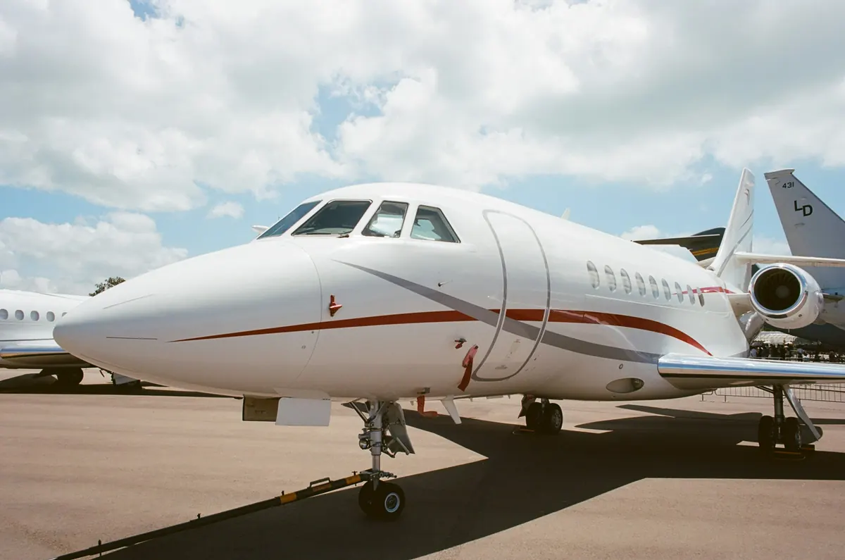 Nose of a white business jet on the ramp under a bright, cloud-streaked sky